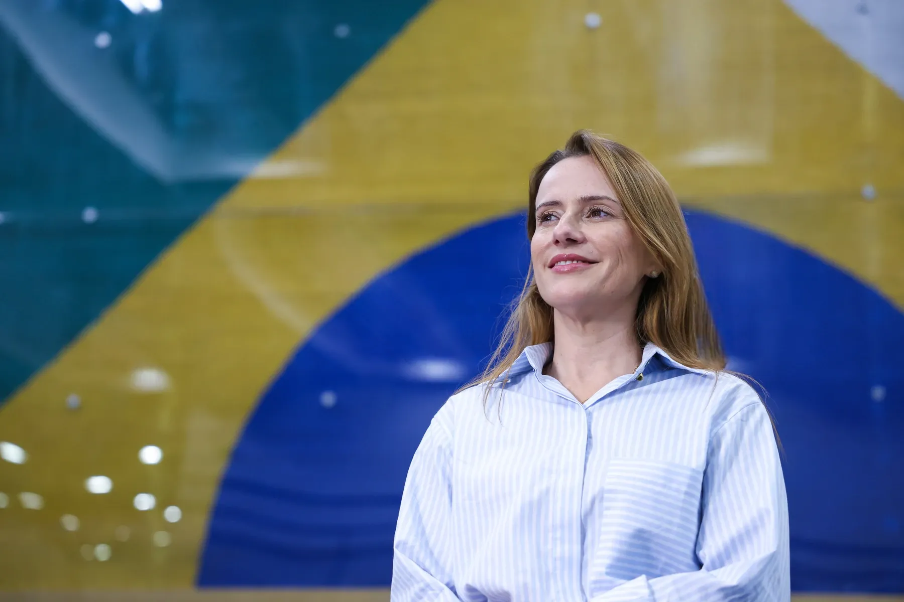 Kátia Dias sorrindo em frente à bandeira do Brasil, durante o mandato na Câmara